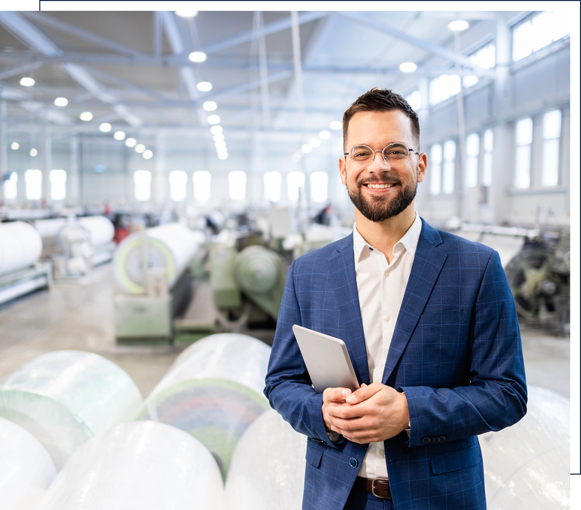 Man in factory holding tablet, smiling.